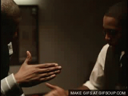 A Man In A Suit And Tie Is Giving Another Man A High Five GIF