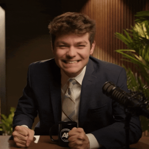 A Man In A Suit And Tie Is Giving The Middle Finger In Front Of A Microphone GIF