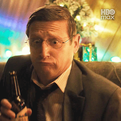 A Man In A Suit And Tie Is Holding A Bottle Of Beer With A Hbo Max Logo In The Background GIF