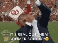 A Man In A Suit And Tie Is Holding A Bottle Of Ketchup While Wearing A Helmet And A Hat . GIF