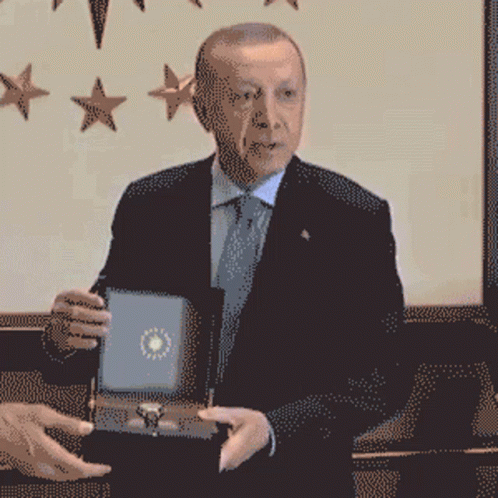 A Man In A Suit And Tie Is Holding A Box GIF