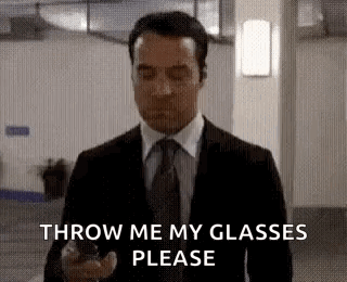 A Man In A Suit And Tie Is Holding A Cell Phone And Asking To Throw Me My Glasses Please . GIF