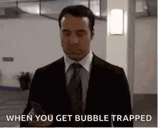A Man In A Suit And Tie Is Holding A Cell Phone And Saying `` When You Get Bubble Trapped '' . GIF