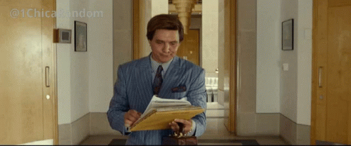 A Man In A Suit And Tie Is Holding A Clipboard And Looking At It GIF