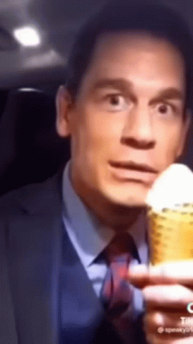 A Man In A Suit And Tie Is Holding A Corn On The Cob And Making A Funny Face . GIF