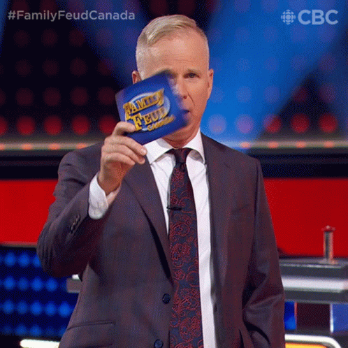 A Man In A Suit And Tie Is Holding A Family Feud Card In Front Of His Face GIF