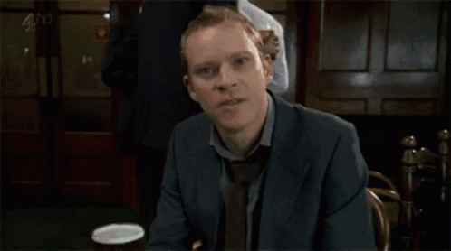 A Man In A Suit And Tie Is Holding A Glass Of Wine GIF