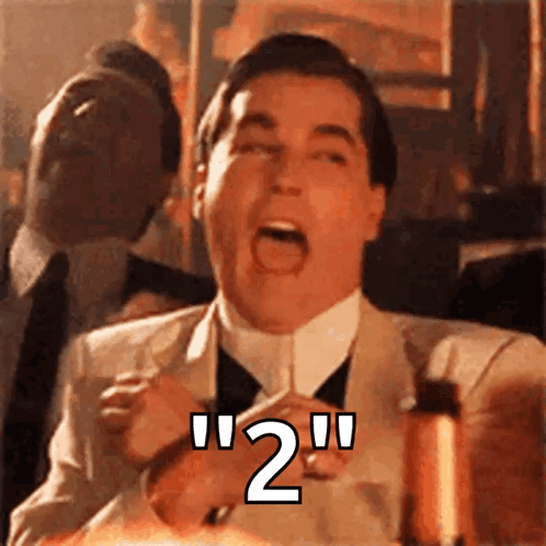 A Man In A Suit And Tie Is Holding A Glass With The Number 2 Written On It . GIF