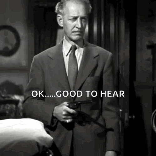 A Man In A Suit And Tie Is Holding A Gun And Says " Ok Good To Hear " GIF