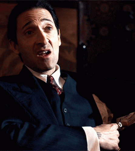 A Man In A Suit And Tie Is Holding A Gun In His Hand GIF