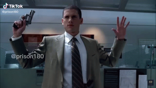 A Man In A Suit And Tie Is Holding A Gun In His Right Hand .. GIF
