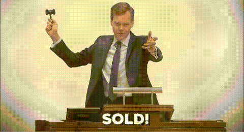 A Man In A Suit And Tie Is Holding A Hammer In Front Of A Podium That Says Sold . GIF