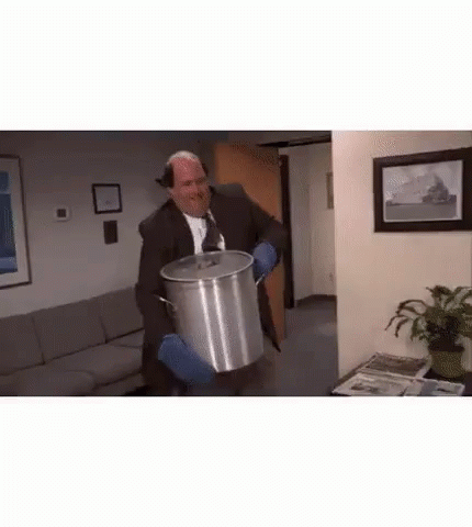 A Man In A Suit And Tie Is Holding A Large Pot . GIF