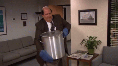 A Man In A Suit And Tie Is Holding A Large Pot In A Waiting Room GIF