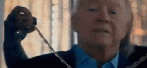 A Man In A Suit And Tie Is Holding A Necklace In His Hand . GIF