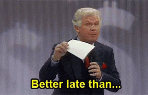 A Man In A Suit And Tie Is Holding A Piece Of Paper And Says `` Better Late Than '' . GIF