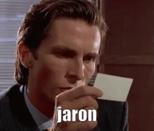 A Man In A Suit And Tie Is Holding A Piece Of Paper In His Hand With The Name Jaron Written On It . GIF