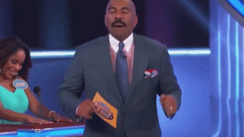 A Man In A Suit And Tie Is Holding A Piece Of Paper That Says Family Feud .. GIF