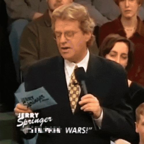 A Man In A Suit And Tie Is Holding A Piece Of Paper That Says " Jerry Springer " On It GIF