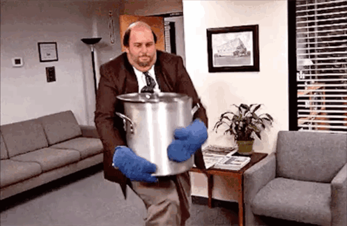 A Man In A Suit And Tie Is Holding A Pot In A Living Room . GIF