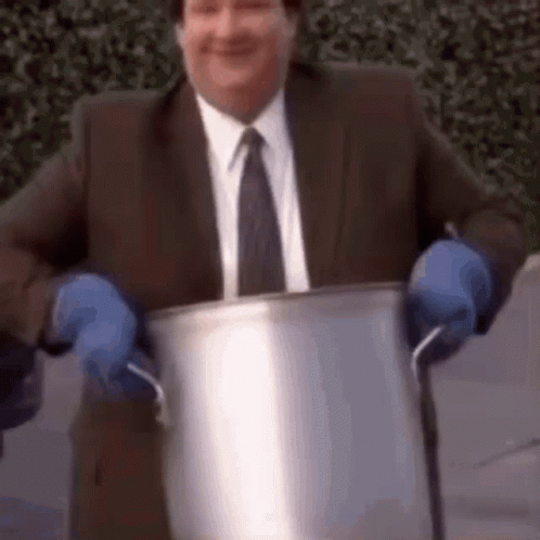 A Man In A Suit And Tie Is Holding A Pot With Blue Gloves On . GIF