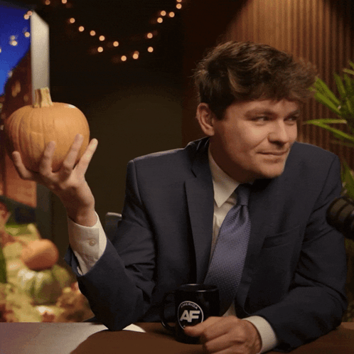 A Man In A Suit And Tie Is Holding A Pumpkin And A Coffee Mug That Says Af GIF