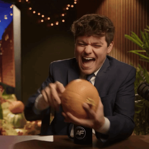 A Man In A Suit And Tie Is Holding A Pumpkin In Front Of A Cup That Says Af GIF