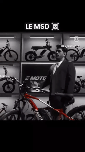 A Man In A Suit And Tie Is Holding A Red Bicycle In Front Of A Wall Of Bikes . GIF