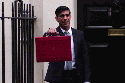 A Man In A Suit And Tie Is Holding A Red Briefcase That Says ' British ' On It GIF