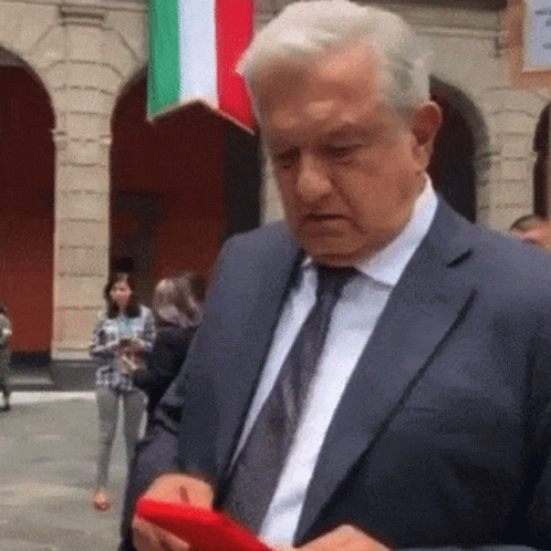 A Man In A Suit And Tie Is Holding A Red Cell Phone . GIF