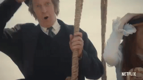 A Man In A Suit And Tie Is Holding A Rope In Front Of A Woman In A White Dress . GIF