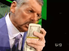 A Man In A Suit And Tie Is Holding A Stack Of Money In Front Of A Tv Screen That Says Usa GIF