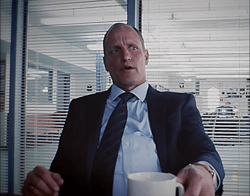 A Man In A Suit And Tie Is Holding A White Cup GIF