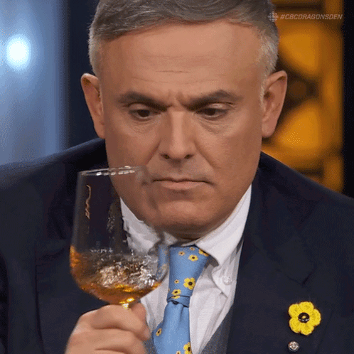 A Man In A Suit And Tie Is Holding A Wine Glass GIF