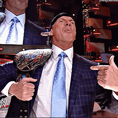 A Man In A Suit And Tie Is Holding A Wrestling Championship Belt Around His Shoulder GIF