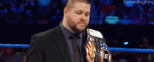 A Man In A Suit And Tie Is Holding A Wrestling Championship Belt In A Ring . GIF