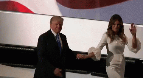 A Man In A Suit And Tie Is Holding Hands With A Woman In A White Dress GIF