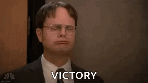 A Man In A Suit And Tie Is Holding His Arms In The Air And Saying Victory . GIF