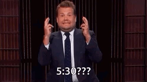 A Man In A Suit And Tie Is Holding His Fingers Crossed And Making A Funny Face . GIF
