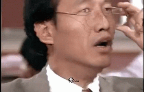 A Man In A Suit And Tie Is Holding His Glasses Up To His Eyes . GIF