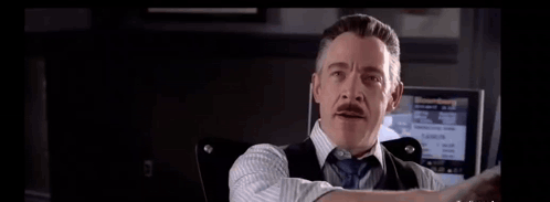 A Man In A Suit And Tie Is Holding His Hand Up In Front Of A Screen . GIF