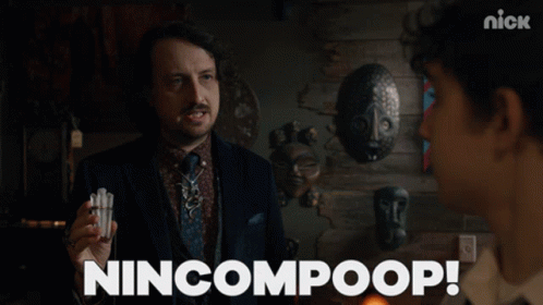 A Man In A Suit And Tie Is Holding Something In His Hand And Says Nincompoop GIF