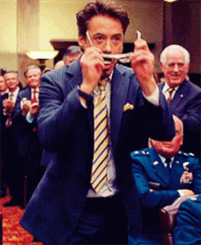 A Man In A Suit And Tie Is Holding Something In His Hand GIF