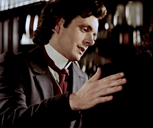 A Man In A Suit And Tie Is Holding Something In His Hands GIF