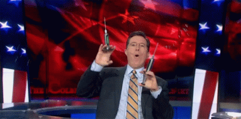 A Man In A Suit And Tie Is Holding Two Syringes In His Hands . GIF
