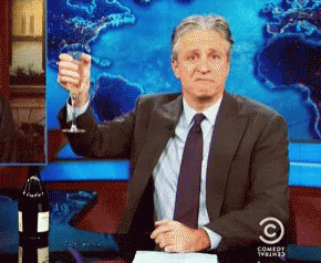 A Man In A Suit And Tie Is Holding Up A Glass Of Wine In Front Of A Comedy Central Logo GIF