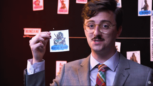 A Man In A Suit And Tie Is Holding Up A Sticker That Says Kotal Karim GIF
