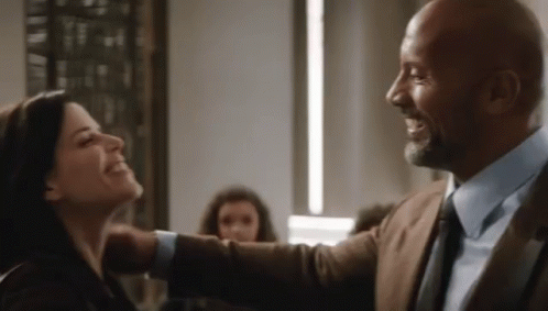 A Man In A Suit And Tie Is Hugging A Woman In A Room And Smiling . GIF