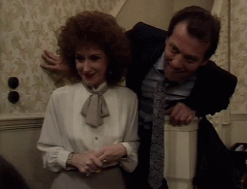 A Man In A Suit And Tie Is Hugging A Woman In A White Blouse GIF
