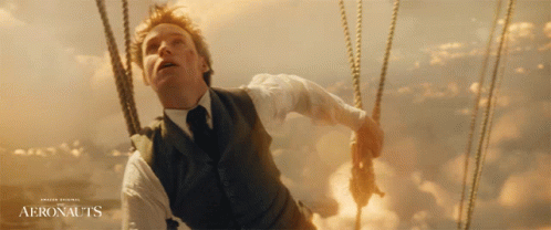 A Man In A Suit And Tie Is In A Hot Air Balloon With The Words Aeronauts On The Bottom GIF